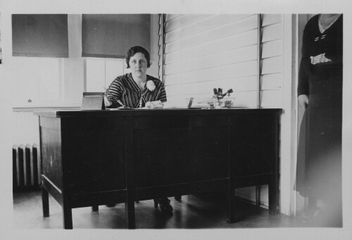 3.26.3: Miss LUna Lewis seated at her desk.